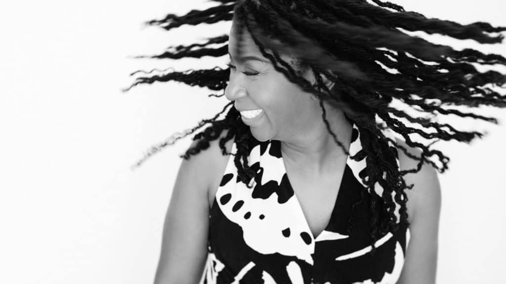 Black and white in-studio portrait of a woman shaking her head, with her hair flying from left to right.